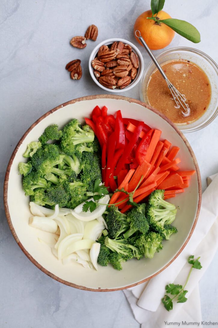 The ingredients for stir fry vegetables are chopped and ready to cook. They sit in a white bowl with a small dish of orange stir fry sauce on the side. 