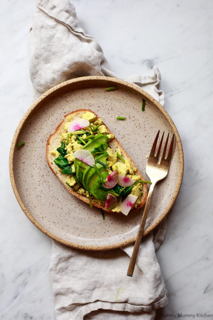A slice of sourdough toast is topped with tofu scramble, watermelon radish, and chives. 