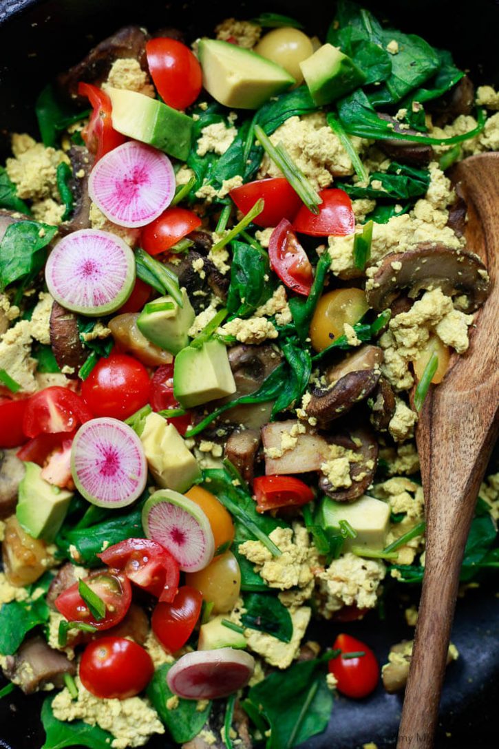 Close-up photo of a vegetable tofu scramble with spinach topped with watermelon radish, avocado, and chives. 