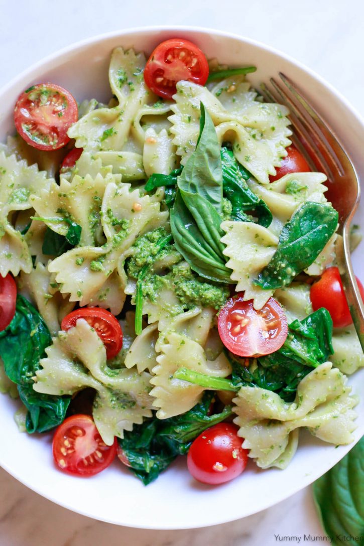 A bowl of vegan pesto pasta made with bowties, cherry tomatoes, spinach and fresh basil pesto. 