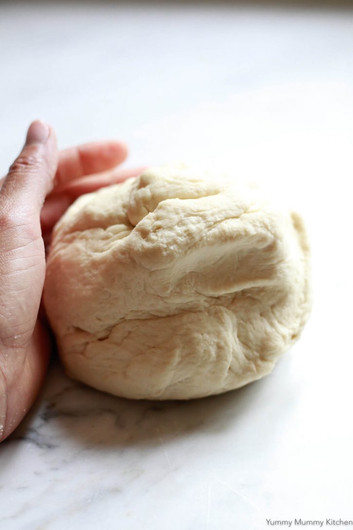 A hand kneads a fresh ball of homemade pizza dough on a marble countertop. 