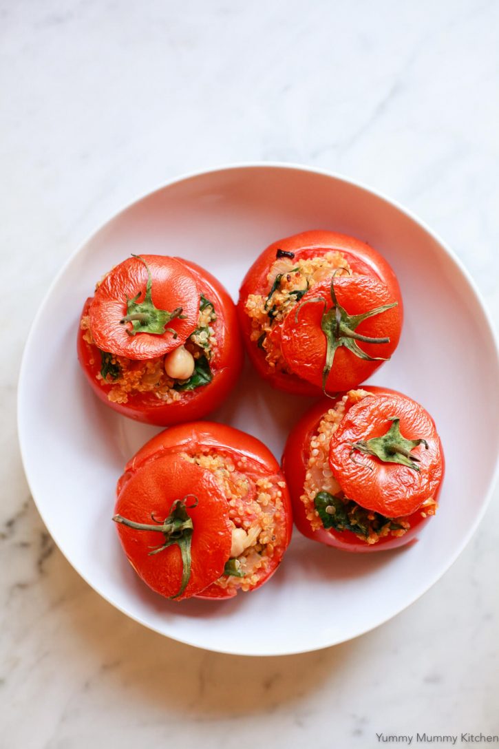 A white bowl filled with four vegetarian stuffed baked tomatoes filled with quinoa, chickpeas, and spinach. 