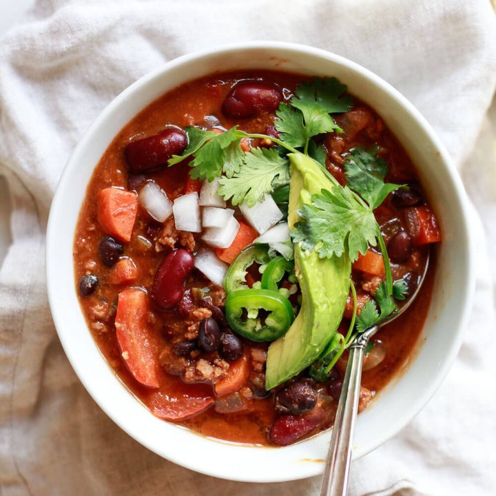 A bowl filled with a hearty vegan chili topped with avocado, cilantro, and jalapeno.
