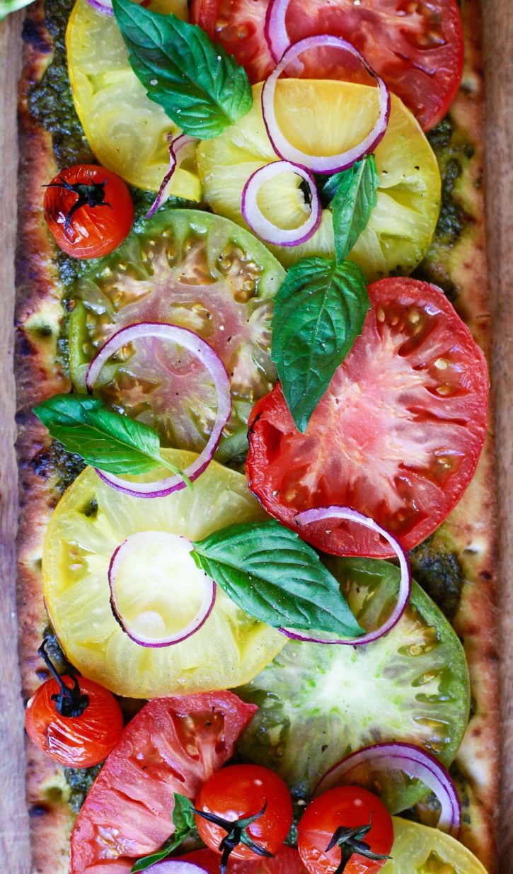 Colorful red, yellow, and green heirloom tomato slices on a pesto pizza. 
