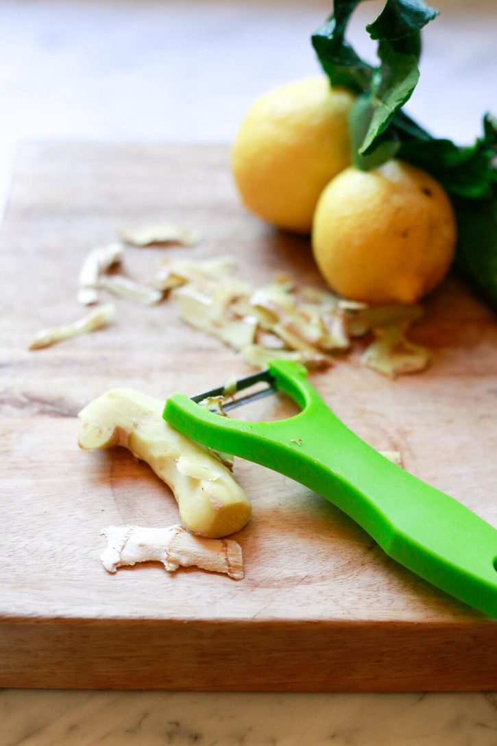 A green vegetable peeler peels a piece of fresh ginger. 