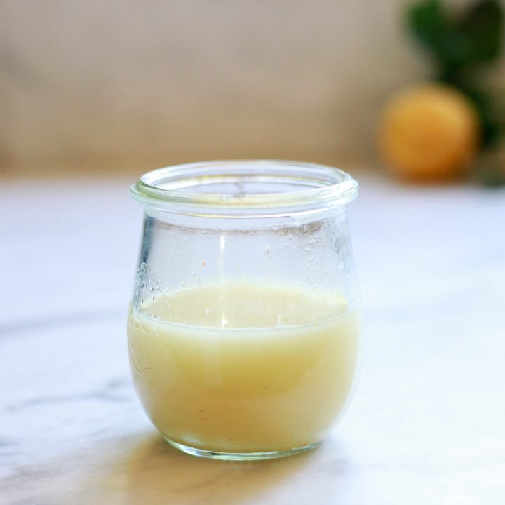 A small jar filled with a ginger shot sits on a countertop.