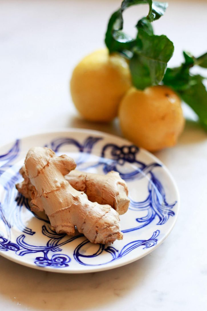 Fresh ginger on a small plate with lemons in the background. These are the ingredients for a ginger shot recipe. 