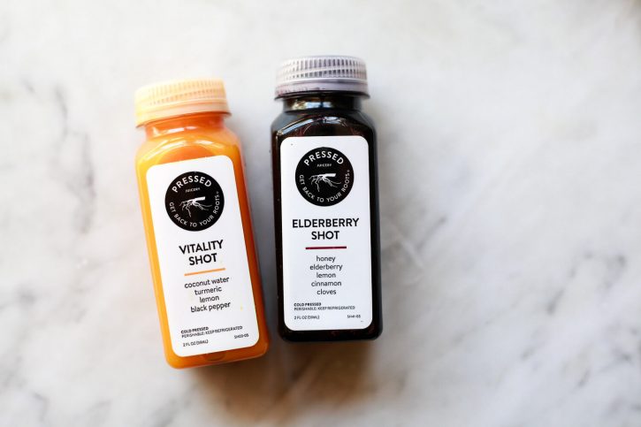 Wellness shots from Pressed Juicery on a marble countertop. Turmeric Vitality shot and Elderberry shot. 