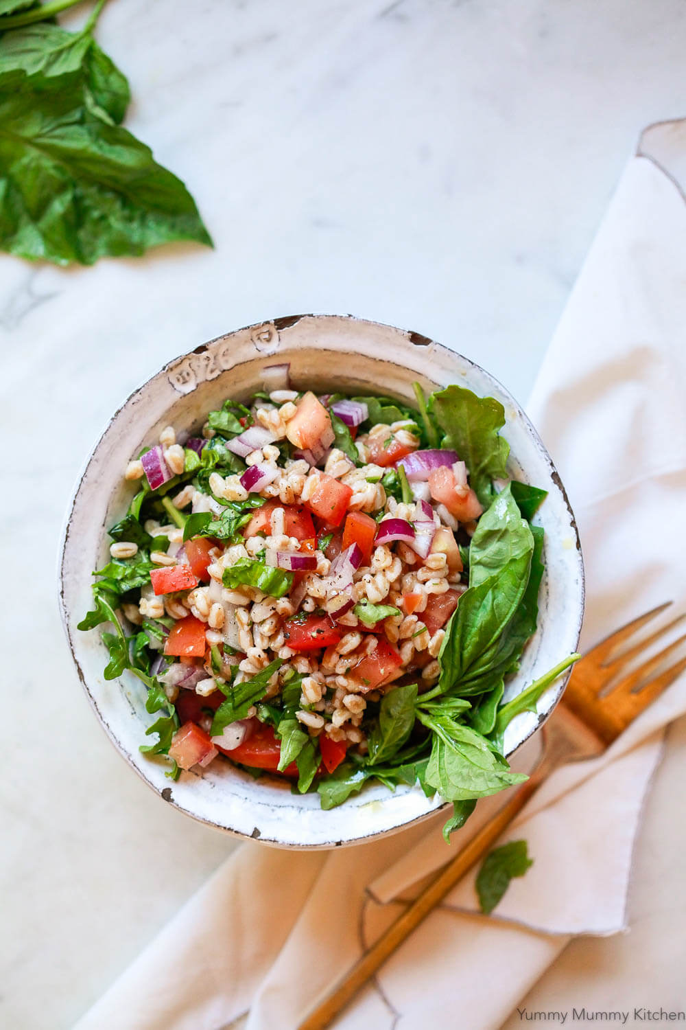 A white ceramic bowl filled with a Tuscan farro salad with tomatoes, red onion, basil, and arugula. 