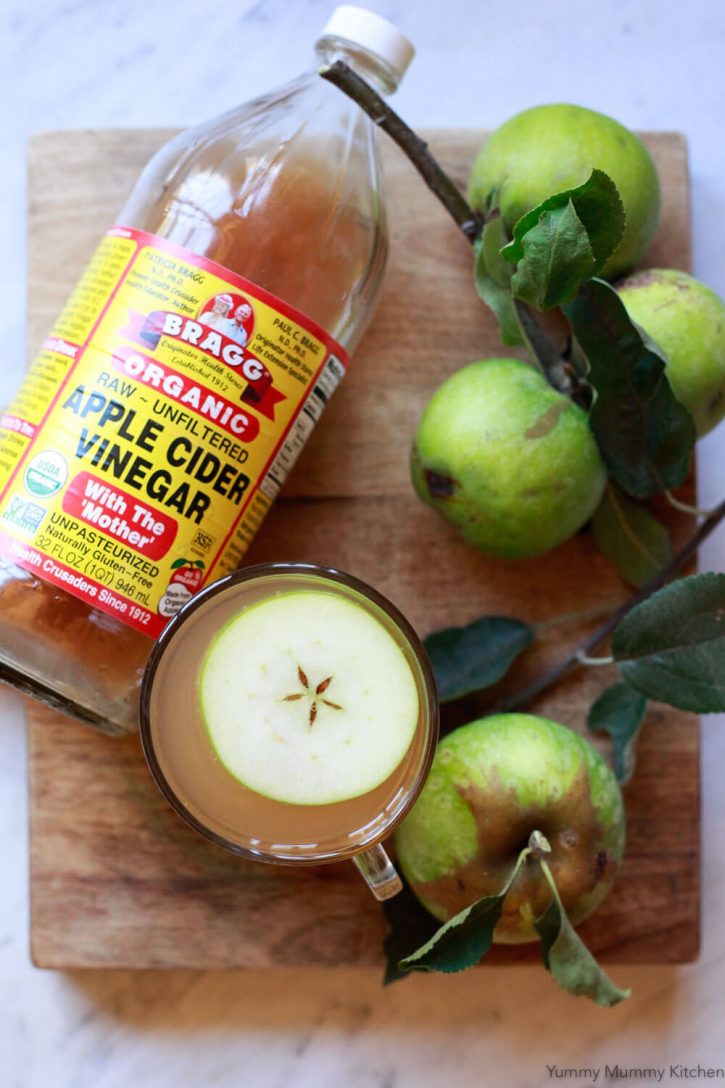 A bottle of Bragg apple cider vinegar sits on a cutting board next to hot apple cider vinegar detox drink. 