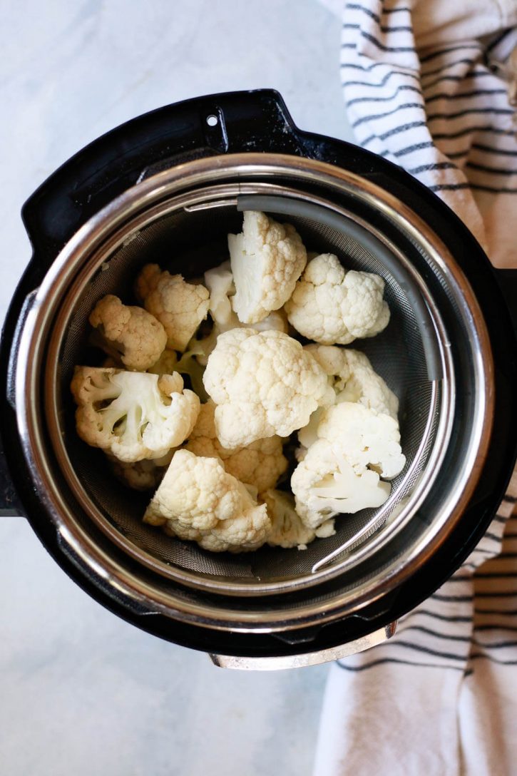 Large cauliflower florets in a steamer basket inside an Instant Pot pressure cooker. 