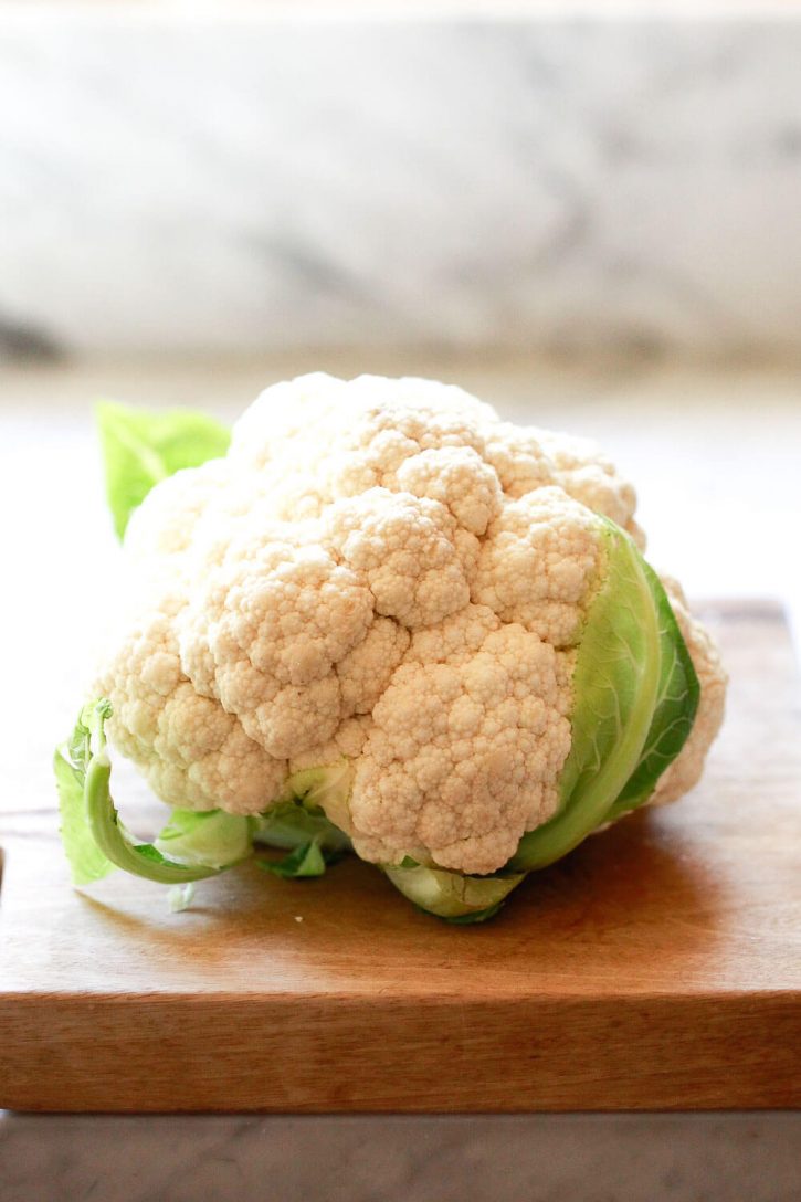 A beautiful head of cauliflower on a cutting board in a white kitchen. This cauliflower is ready to be cut into florets and steamed for cauliflower mash. 