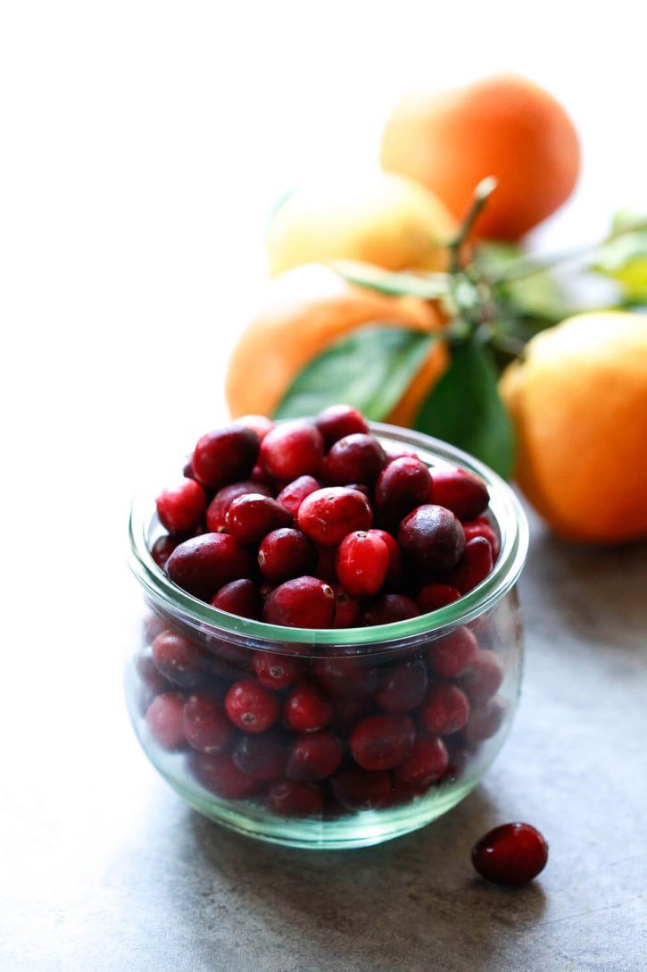 A bowl of fresh cranberries with oranges in the background. These are the main ingredients in a Cranberry Orange Sauce Recipe. 