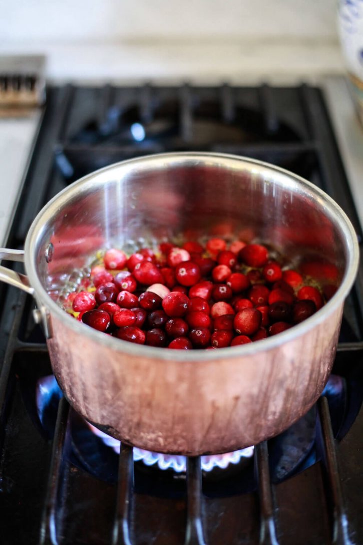 Fresh cranberries are added to a saucepan of orange juice and sugar to make cranberry orange sauce for Thanksgiving. 