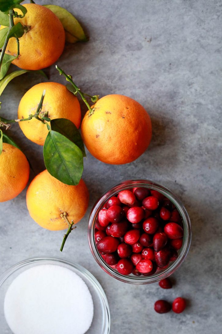 Oranges, fresh cranberries, and zero carb keto sugar free monk fruit sweetener on a countertop. These are the ingredients for a sugar free or keto cranberry sauce. 