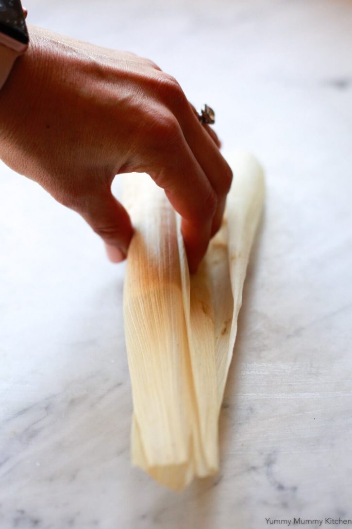 A corn husk is wrapped over tamale filling. An image showing how to wrap tamales. 