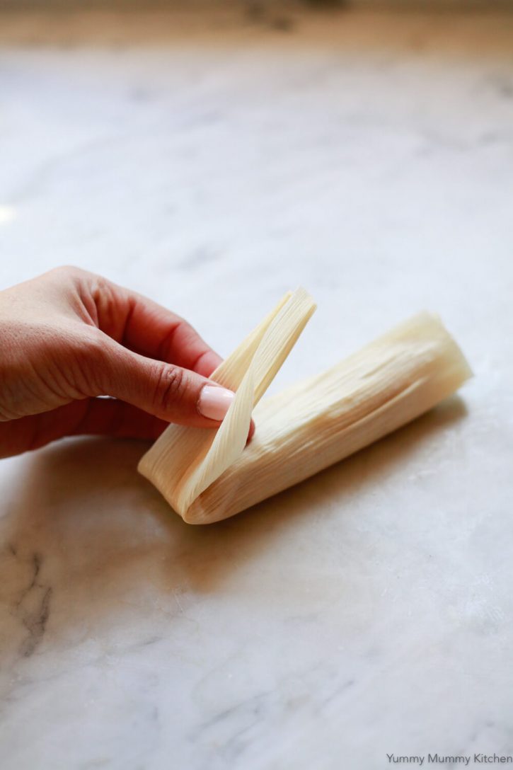 The bottom of a corn husk is folded over a tamale to demonstrate how to wrap a tamale. 