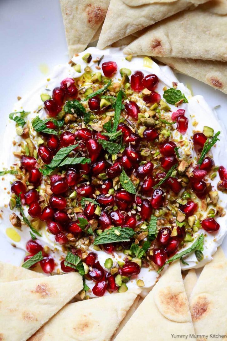 A beautiful dish of labneh cheese topped with za'atar, pomegranate, pistachios, and mint served with pita bread. 