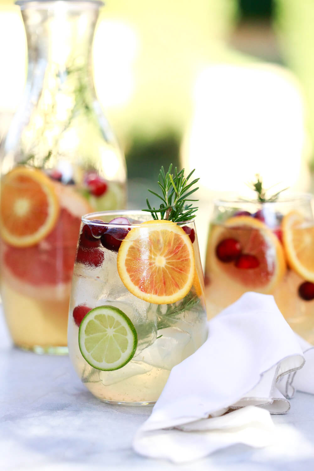 Two stemless wine glasses filled with citrus white wine sangria on an outdoor table. 