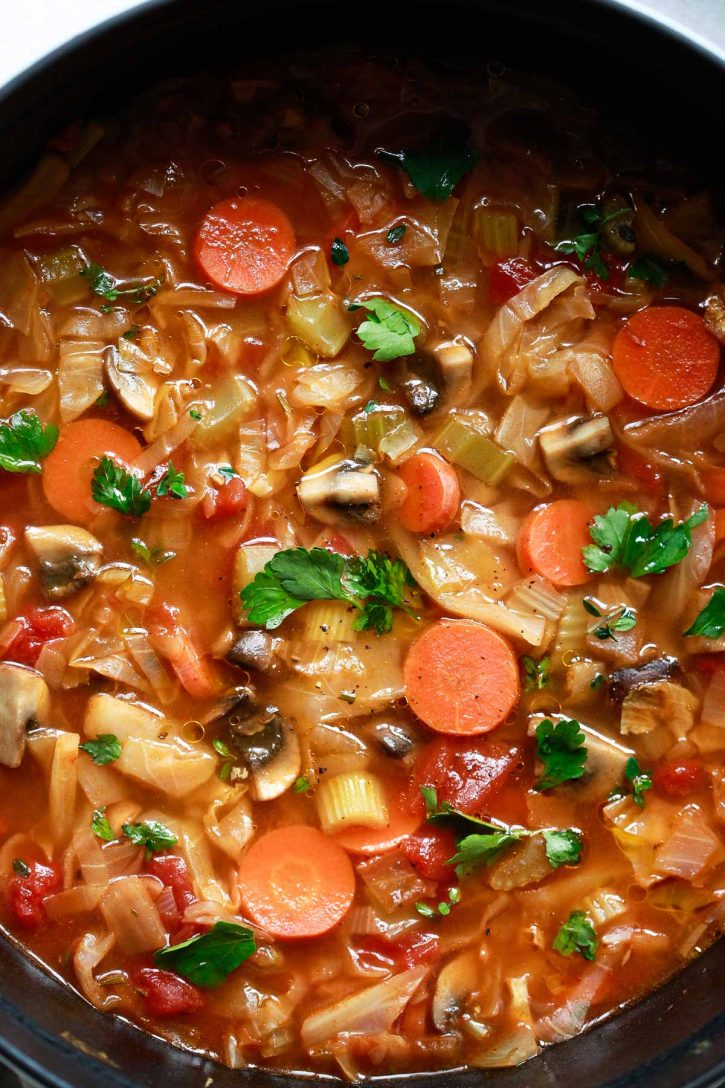 A close-up photo of cabbage soup with carrots, celery, mushrooms, tomatoes, and cabbage is garnished with parsley. A beautiful weight loss soup recipe. 