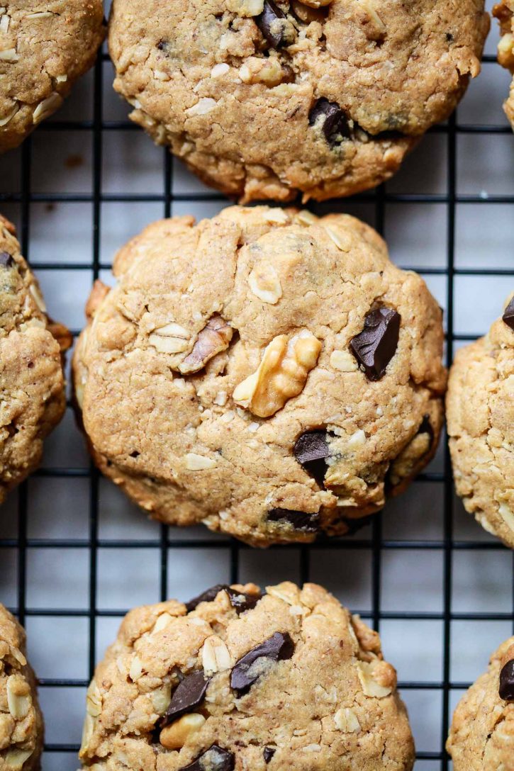 A close-up photo of peanut butter cowboy cookies with oats, chocolate, and walnuts on a cooling rack. 