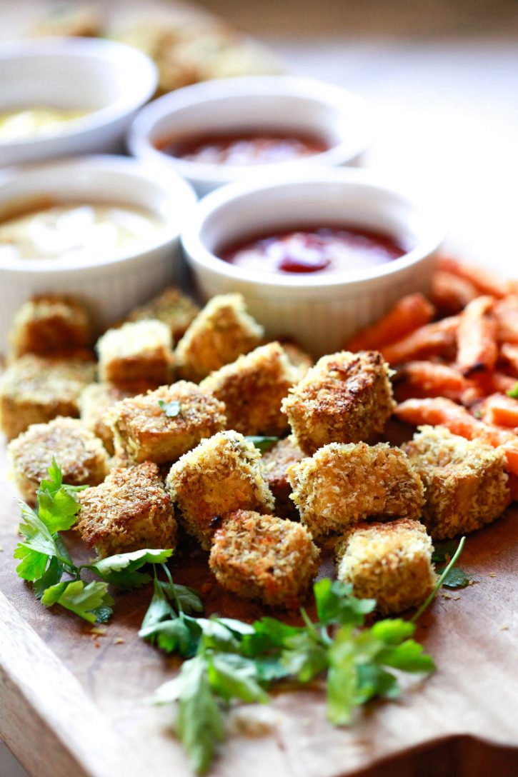 Crispy panko crusted baked tofu nuggets on a wooden platter with ketchup and sweet potato fries. 