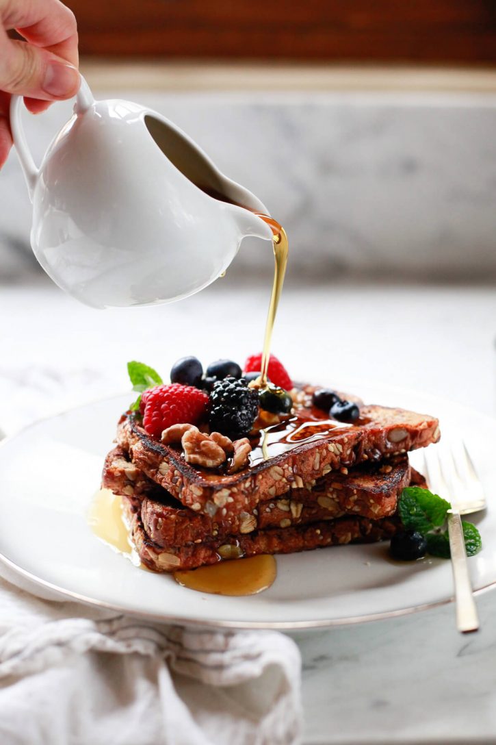 Maple syrup is poured over a stack of vegan french toast with berries. 
