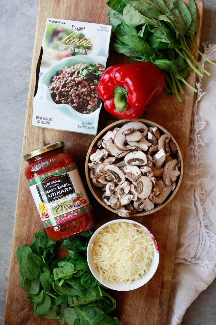 Trader Joe's steamed lentils, marinara, bell pepper, sliced mushrooms, basil, and cheese sit on a cutting board. These are the ingredients for a vegetarian lentil casserole. 