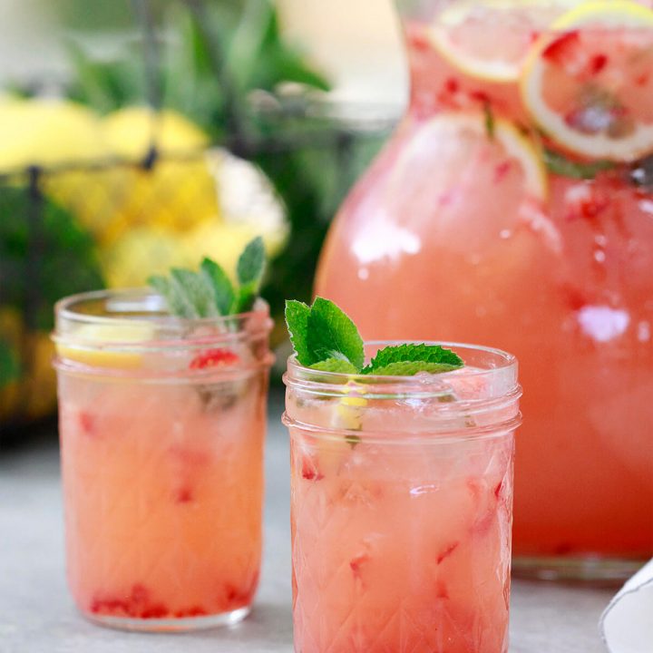 A pitcher and two glasses filled with homemade strawberry pink lemonade.