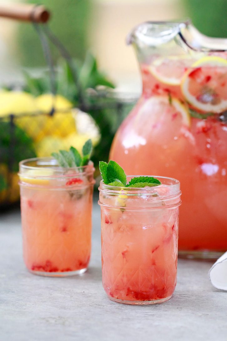 Homemade Strawberry Lemonade Two glasses and a pitcher filled with homemade blended strawberry lemonade sit on a table outside.