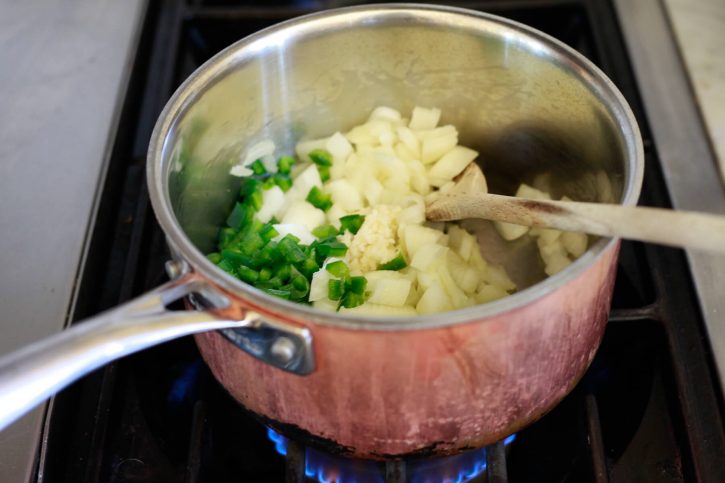 Onions, garlic, and jalapenos saute in a saucepan on the stove. 