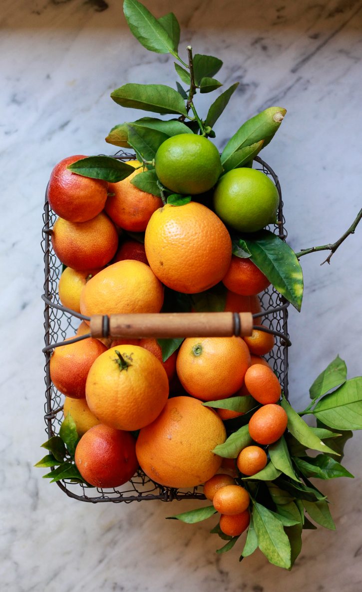 Beautiful photograph of a basket filled with homegrown citrus including oranges, blood oranges, and limes. 