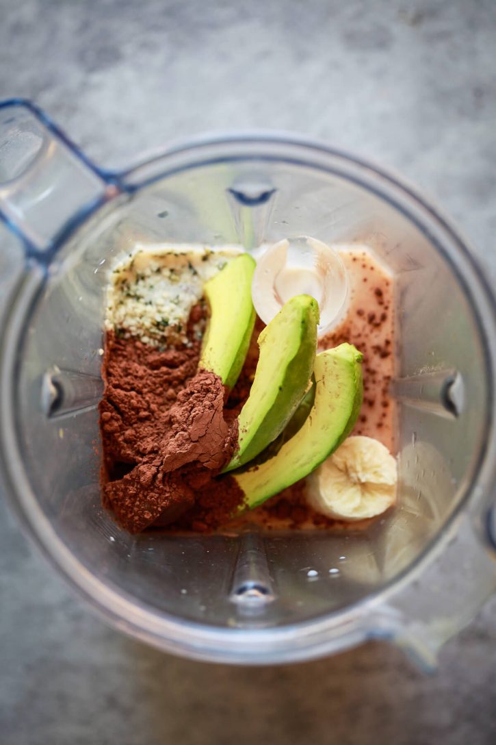 A Vitamix blender is filled with the ingredients for a healthy chocolate banana avocado smoothie. 