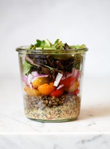 A layered mason jar salad recipe with lentils, tomatoes, onions, and lettuce.
