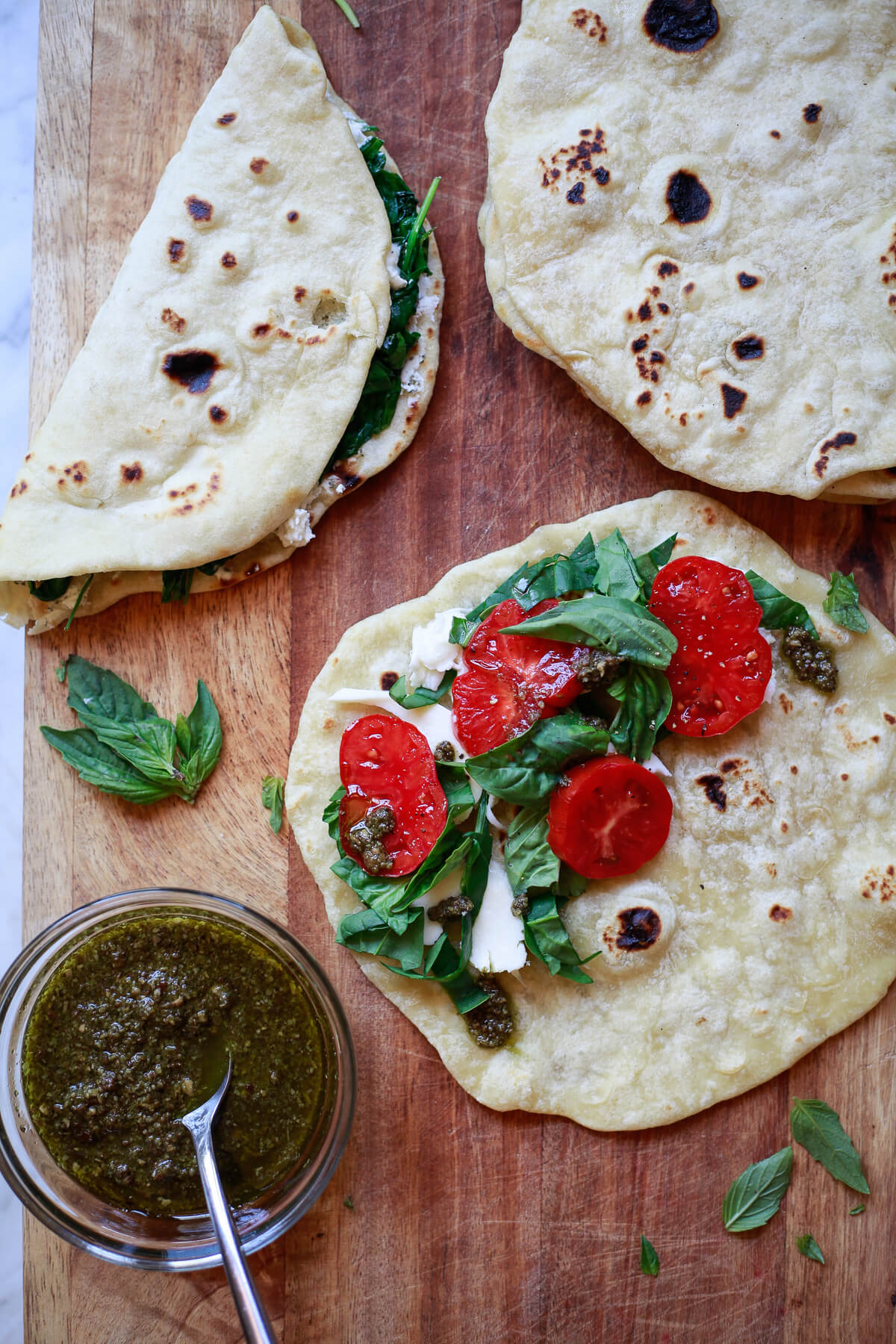 Grilled Piadina Italian flatbread on a cutting board. The flatbreads are topped with mozzarella, tomatoes, and pesto. 