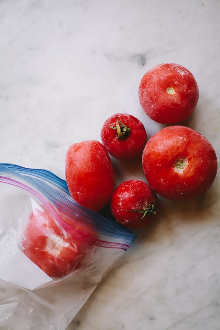 Frozen whole tomatoes come out of a ziplock bag. 