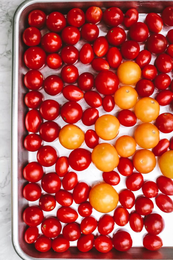Whole fresh cherry tomatoes sit on a sheet pan before going into the freezer. This is the first step in how to freeze cherry tomatoes. 