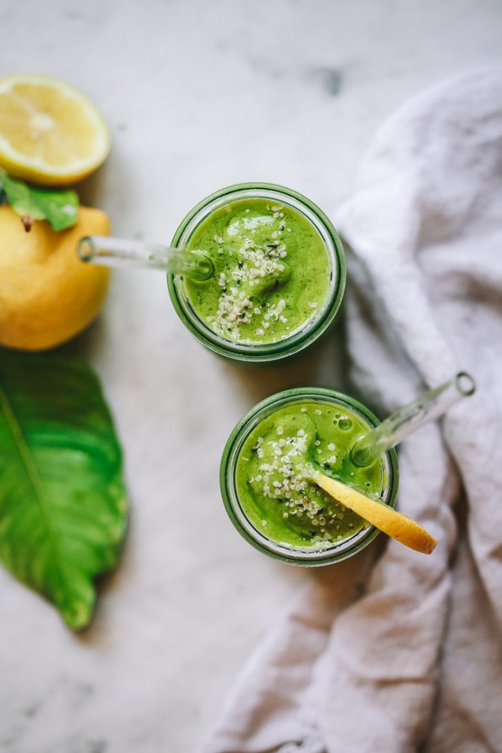Two bright green smoothies topped with hemp seeds sit on a marble countertop with lemons in the background. Beautiful, healthy, green weight loss smoothies. 