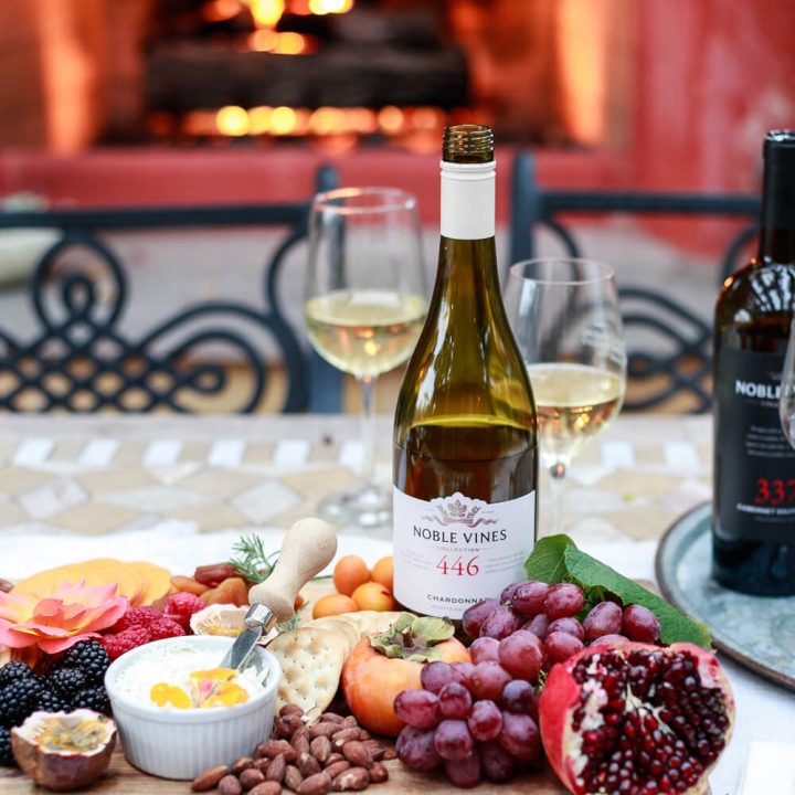 Wine and a charcuterie board on an outdoor table in front of a fire.