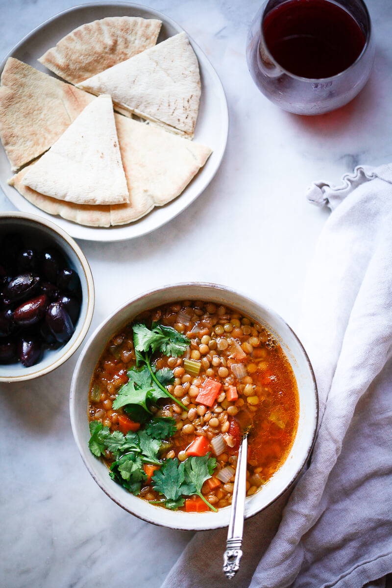 An overhead photo of Greek lentil soup next to olives, pita bread and wine. A great example of Mediterranean Diet recipes. 