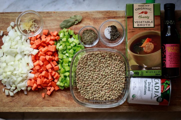 The ingredients for Greek lentil soup sit on a cutting board. 