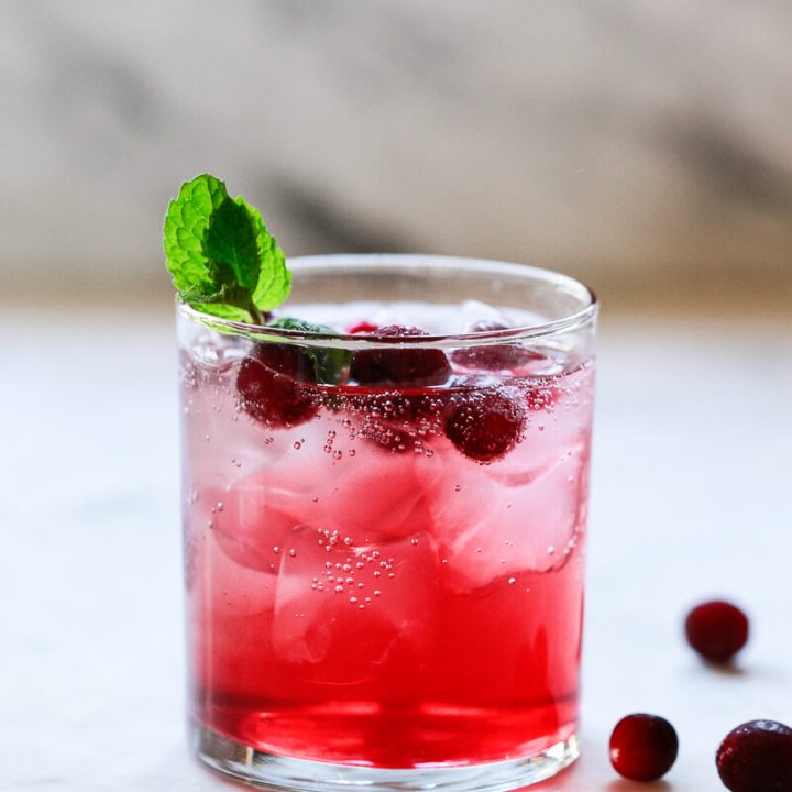A red cranberry detox water drink in a clear glass with ice and cranberries.