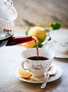 A teapot pours homemade elderberry tea into a teacup.