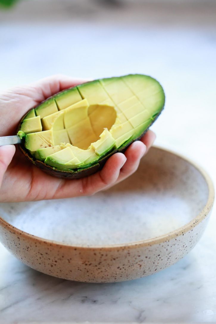 Close-up of a spoon scooping avocado cubes out of the skin into a bowl. 