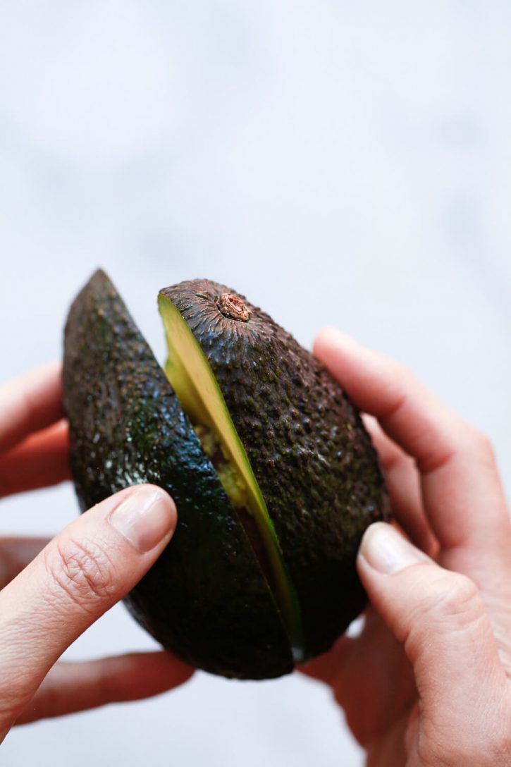 Close-up photography of hands twisting avocado halves apart. 