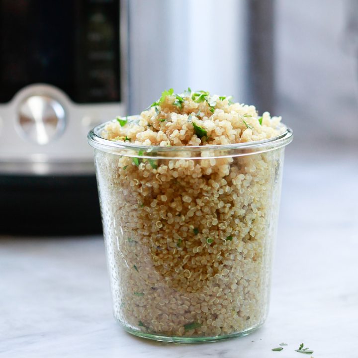 A glass jar filled with perfectly cooked quinoa topped with herbs. An Instant Pot in the background.