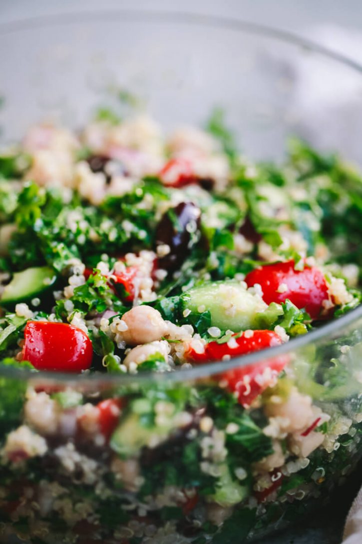 A close-up photo of a quinoa salad with kale, chickpeas, tomatoes, cucumbers, olives, and herbs. 