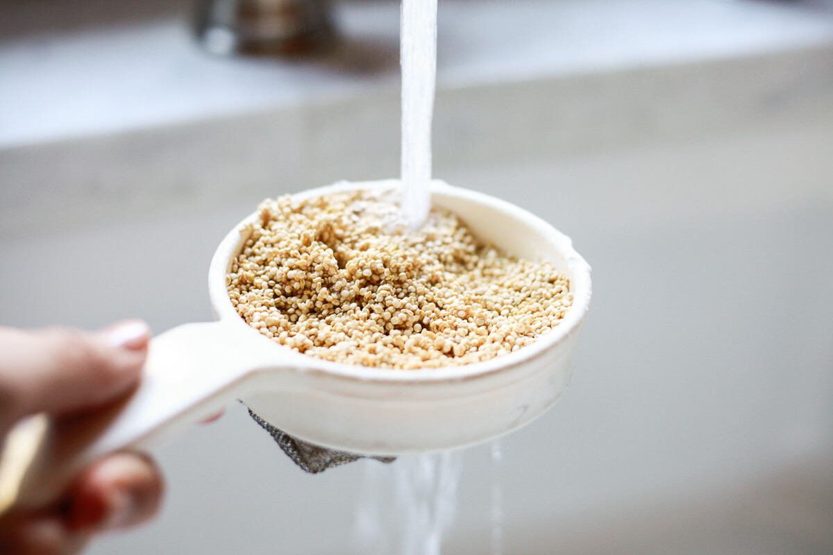 Quinoa in a fine mesh sieve getting rinsed under a kitchen faucet.
