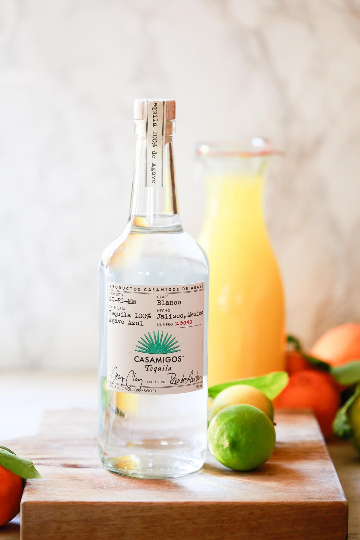 A bottle of clear Casamigos tequila blanco sits on a cutting board in a white kitchen. 
