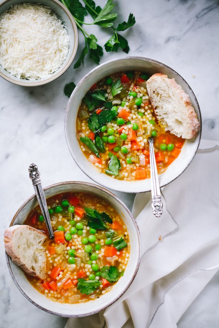Two bowls of pastina soup with peas, carrots, broth, and arancini di pepe pasta. 